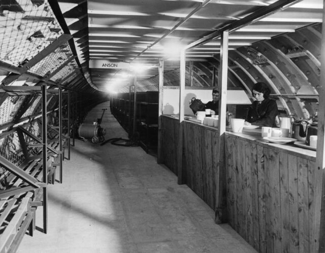 A shot of the inside of a WWII bunker, two women serving tea.